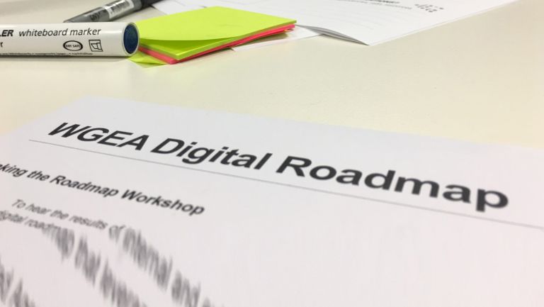 Image of area of tabletop with markers and sticky notes and part of a page titled "WGEA Digital Roadmap"